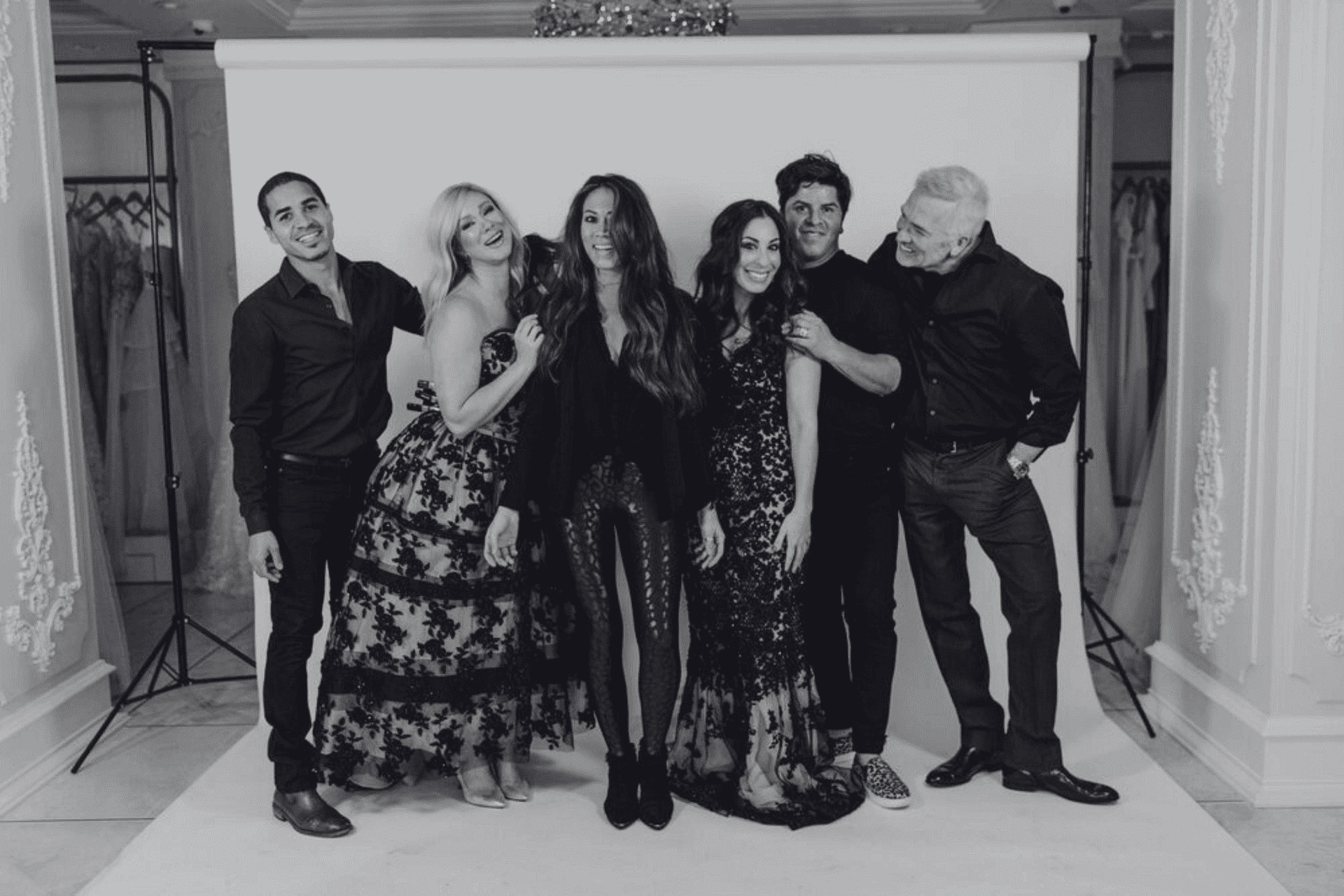 Group of six people posing happily in a photography studio setting with elegant decor.